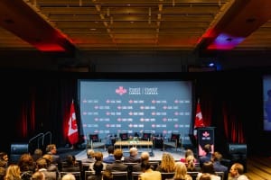 A conference hall with an audience facing a stage set for a panel discussion under the "invest in Canada" banner, captured through event photography.