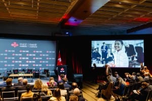 Panel discussion at an invest in Canada event with audience and large screen displaying promotional image, captured by professional event photography.