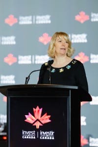 A person delivering a speech at a podium with the "invest in Canada" logos in the background during an event photography session.