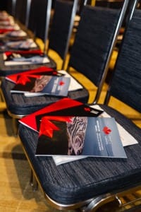 Conference chairs arranged in a row with informational brochures and red ribbons placed on the seats, ready for event photography.