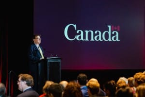 A speaker at a podium with the word "Canada" projected on a screen behind him during an event photography session.