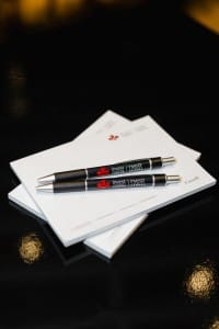 Two pens resting on a stack of documents related to event photography, with the word "invest" printed on them.