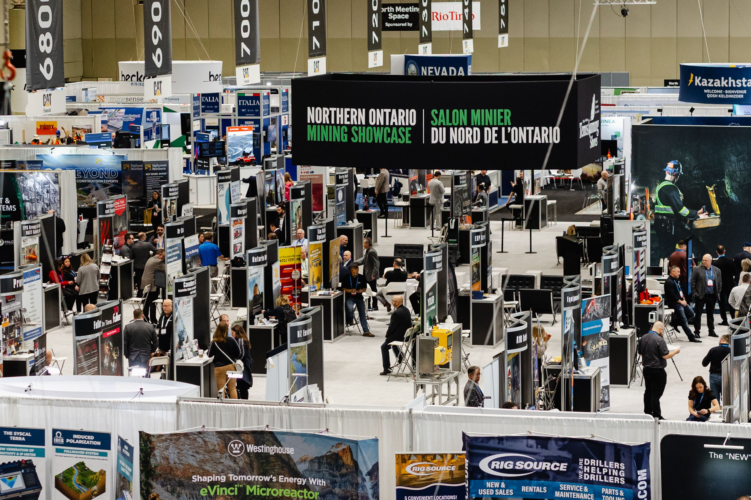 Exhibition hall at a mining industry event with various company booths, corporate photography, and attendees.