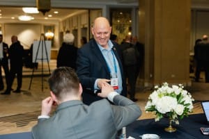 A man is shaking hands with another man at a table during an event photography session.