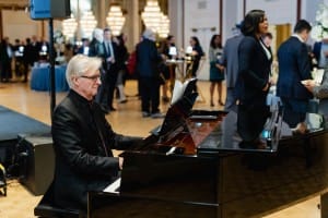A man playing a piano in a room full of people at an event photography session.