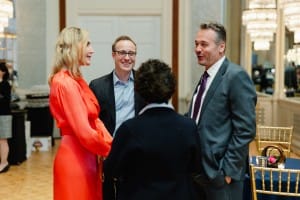 A woman in a red dress is talking to a man in a suit during an event photography session.