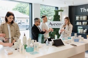 People examining skincare products in a well-lit store with Aveeno branding in the background, captured with a touch of corporate photography finesse.