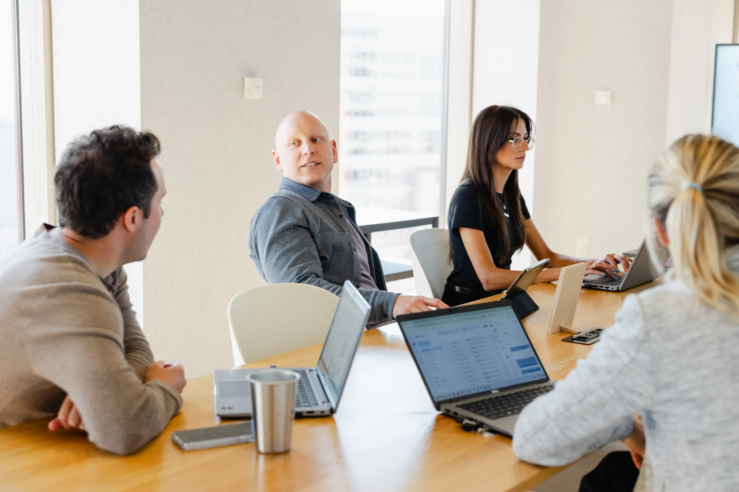 Four people sit around a table with laptops, engaged in a discussion in a bright, modern office.