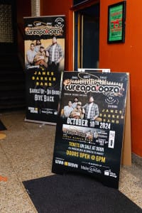 Promotional posters for the "Cureapalooza" social event featuring the James Barker Band on October 10th, 2024, are beautifully showcased near a staircase. Capture the excitement with vibrant social event photography that brings this memorable night to life.