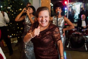 Woman smiling and giving a thumbs-up at a festive event, with a band playing in the background.