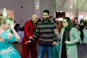 People dancing in a brightly lit room, with some wearing colorful outfits.