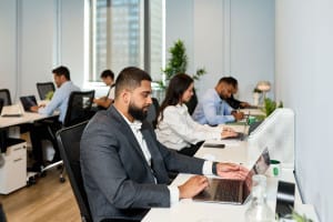 Several people work on laptops at desks in a modern office setting, capturing the essence of event photography with every candid moment and dynamic interaction.
