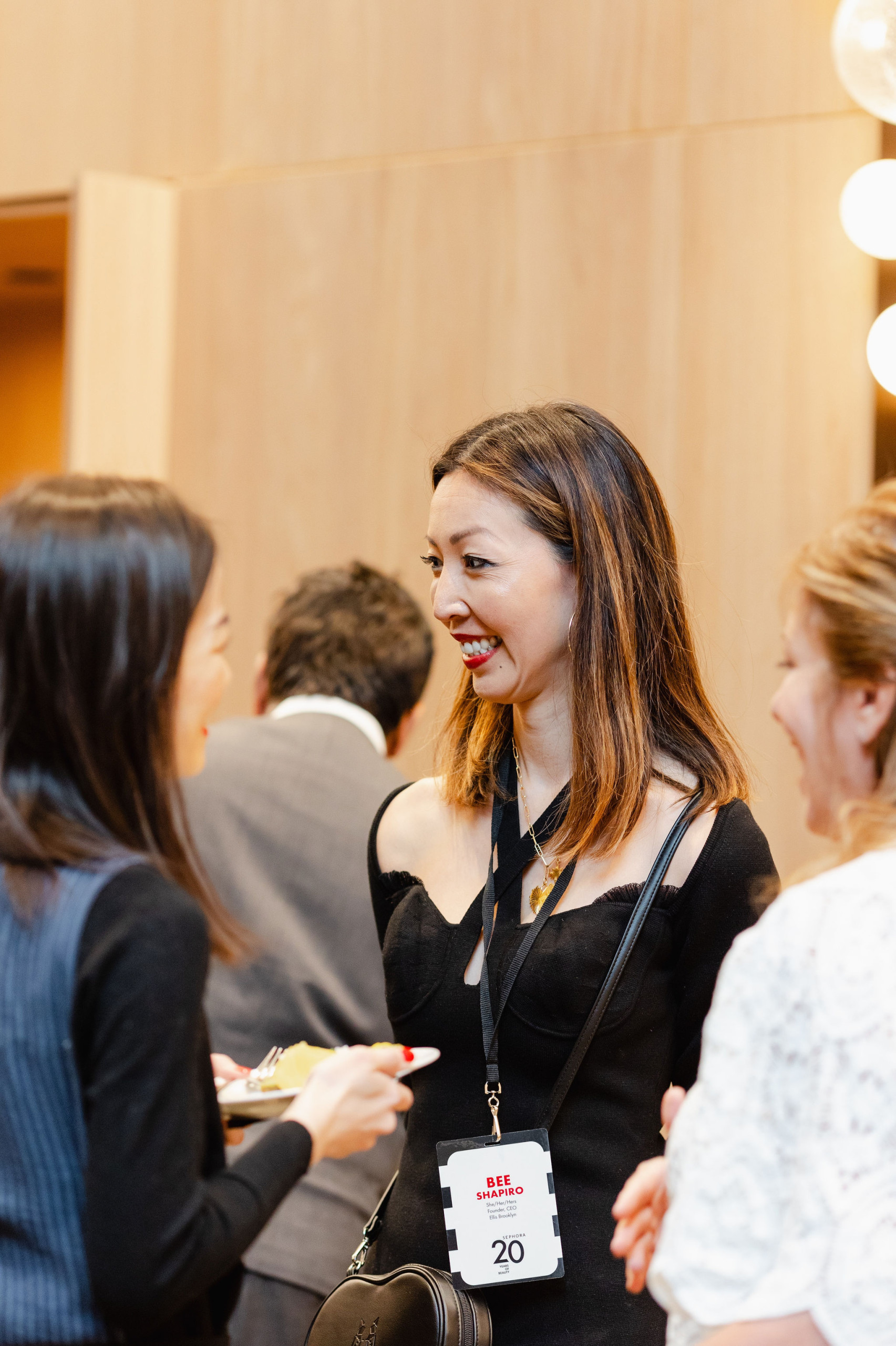 A group of people mingle at an event, one holding a plate. The atmosphere buzzes with networking energy, and an event badge is visible on a woman's outfit—a perfect moment for brand photography to capture the essence of the occasion.