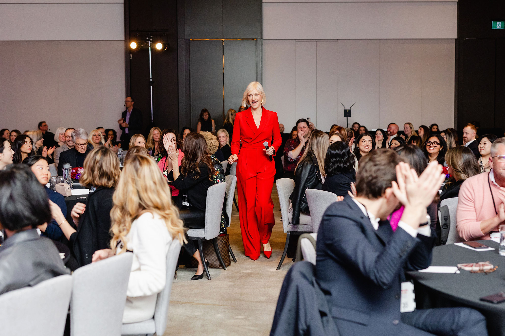 A person in a red suit strolls through a seated crowd at an event, creating moments perfect for brand photography.