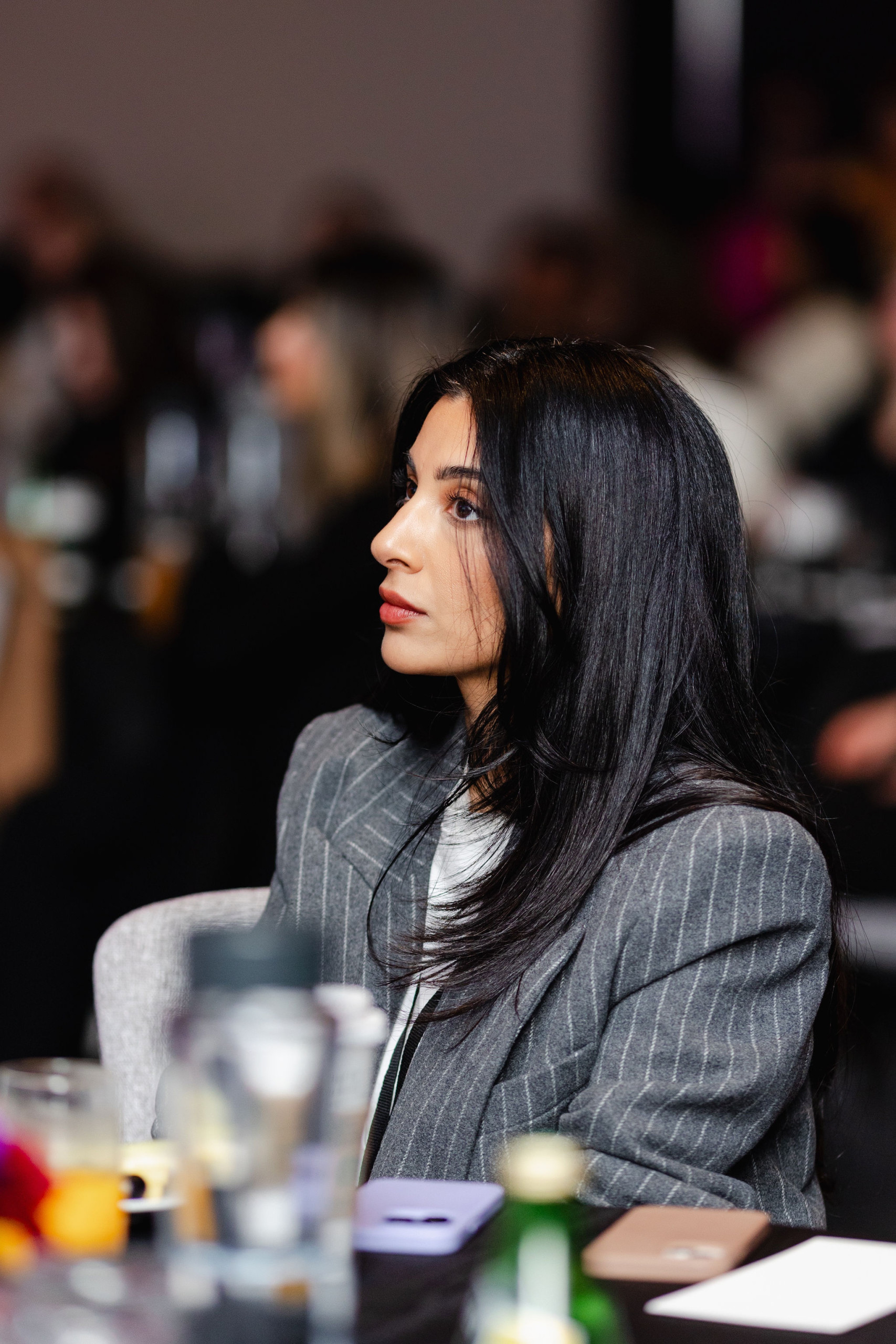 A person with long dark hair sits attentively in a meeting, exuding professionalism in a gray pinstripe blazer, capturing the essence of brand photography.