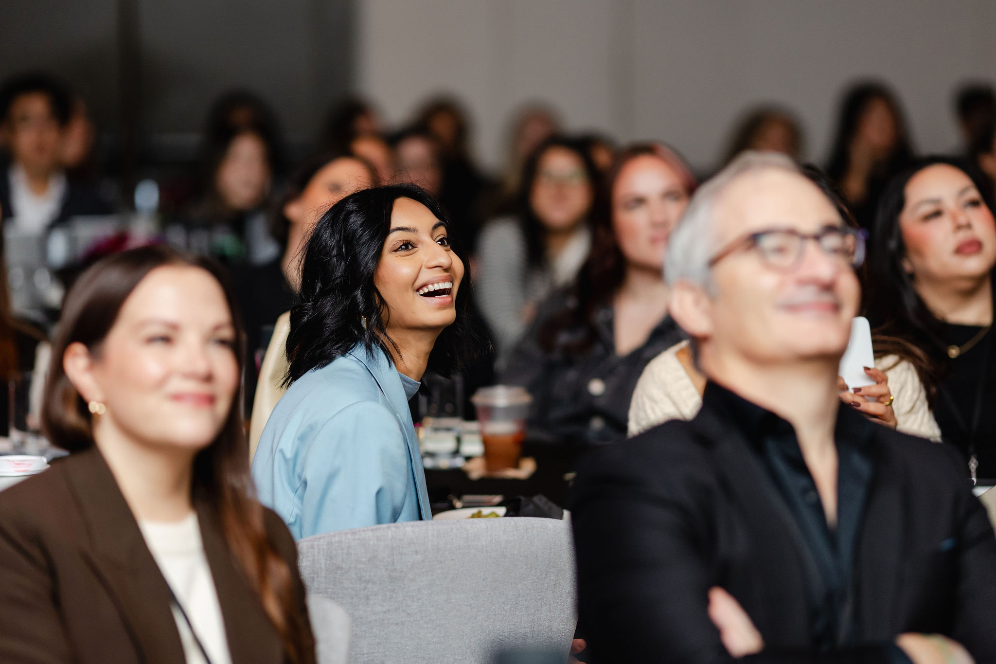 A group of people seated indoors, their faces lit with interest and enjoyment, as they attentively watch something out of frame—an ideal moment for brand photography.