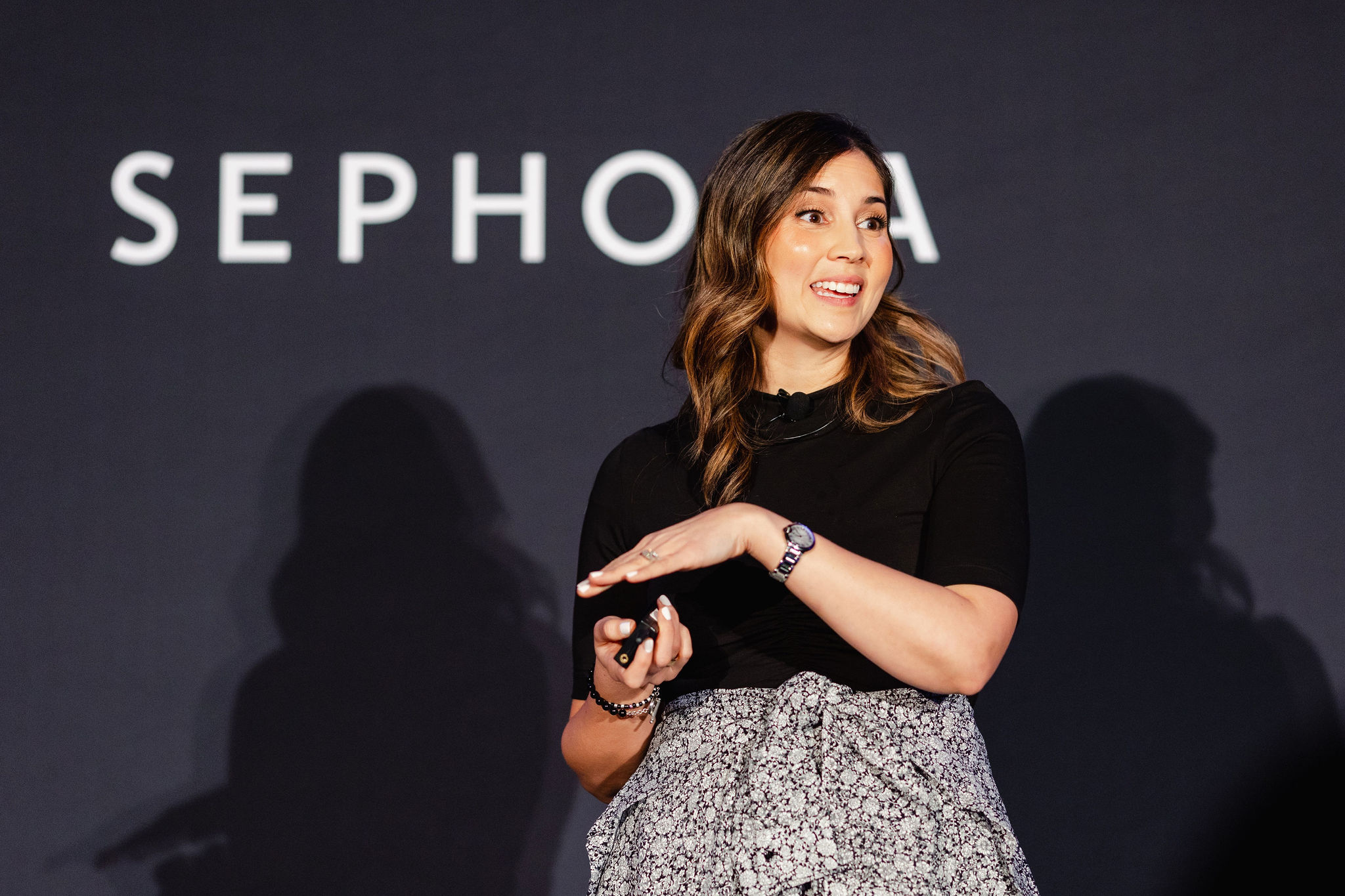 A woman speaks on stage holding a clicker, with the word "Sephora" partially visible in the background, capturing a moment of brand photography.