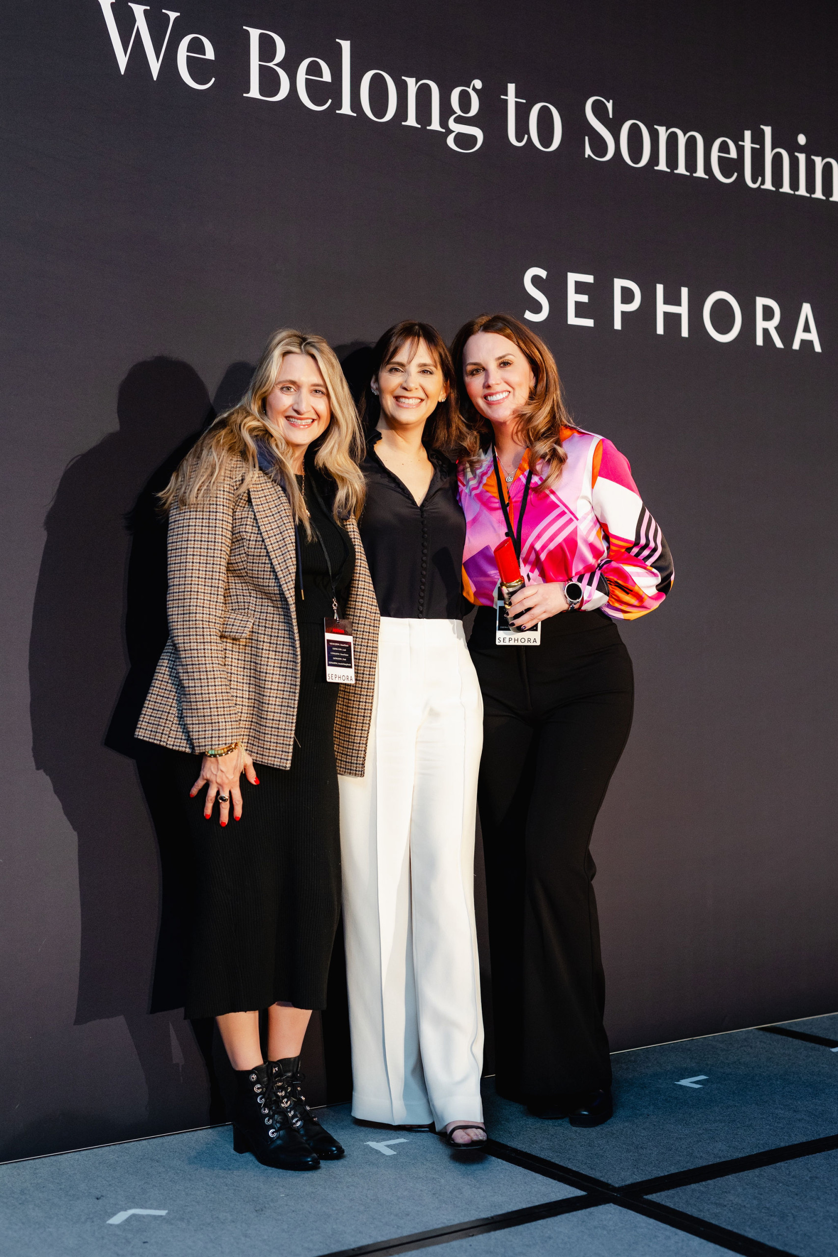 Three women pose confidently in business-casual attire against a Sephora backdrop, capturing the essence of brand photography.
