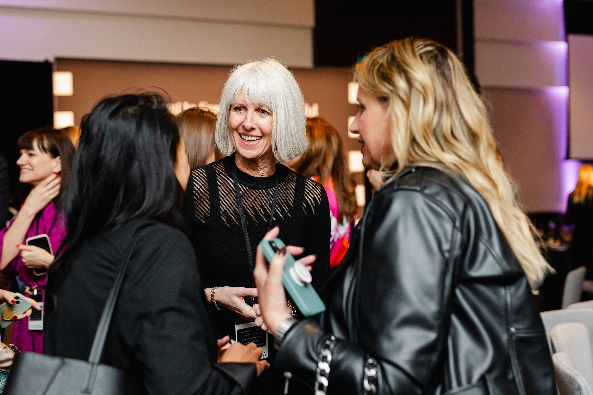 A group of people engaged in lively conversation at an indoor event, with one person in a sleek black outfit capturing attention at the center, embodying the essence of brand photography.