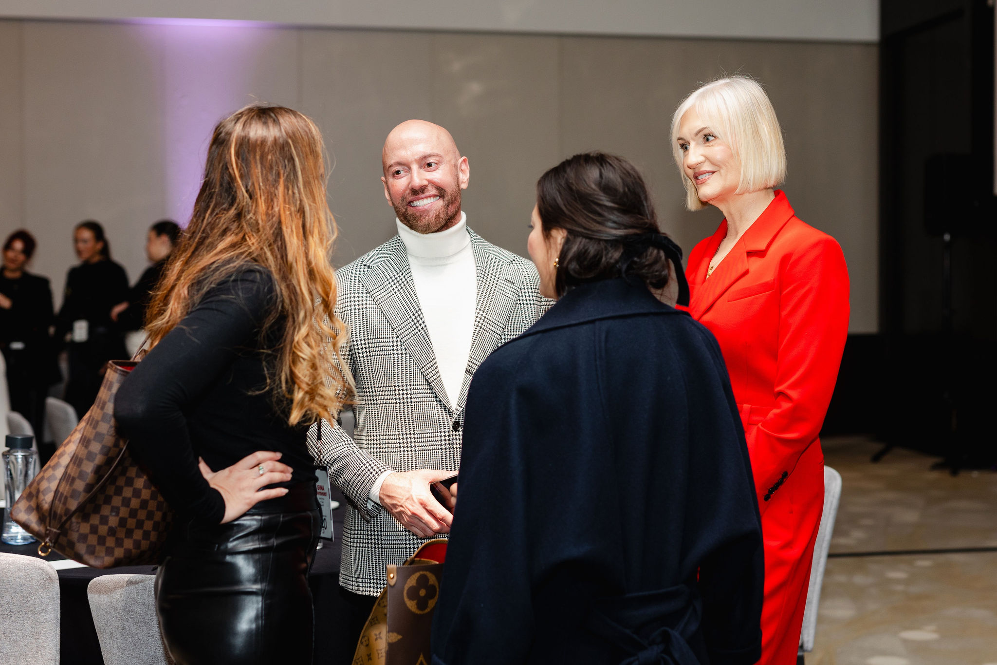 A group of four people in formal attire are standing and engaging in lively conversation at an indoor event, perfectly capturing the essence of brand photography.