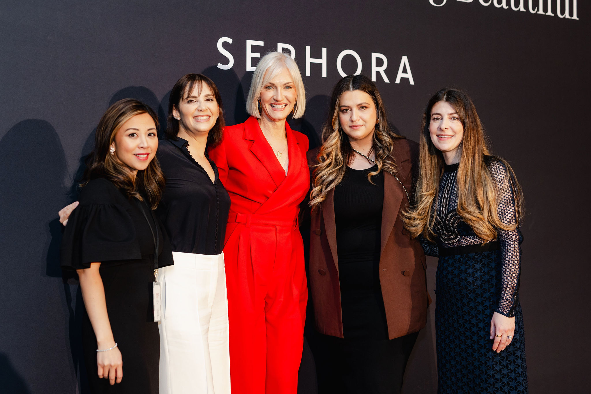 Five women confidently stand together in front of a black backdrop, embodying the essence of brand photography with the word "Sephora" elegantly displayed behind them.