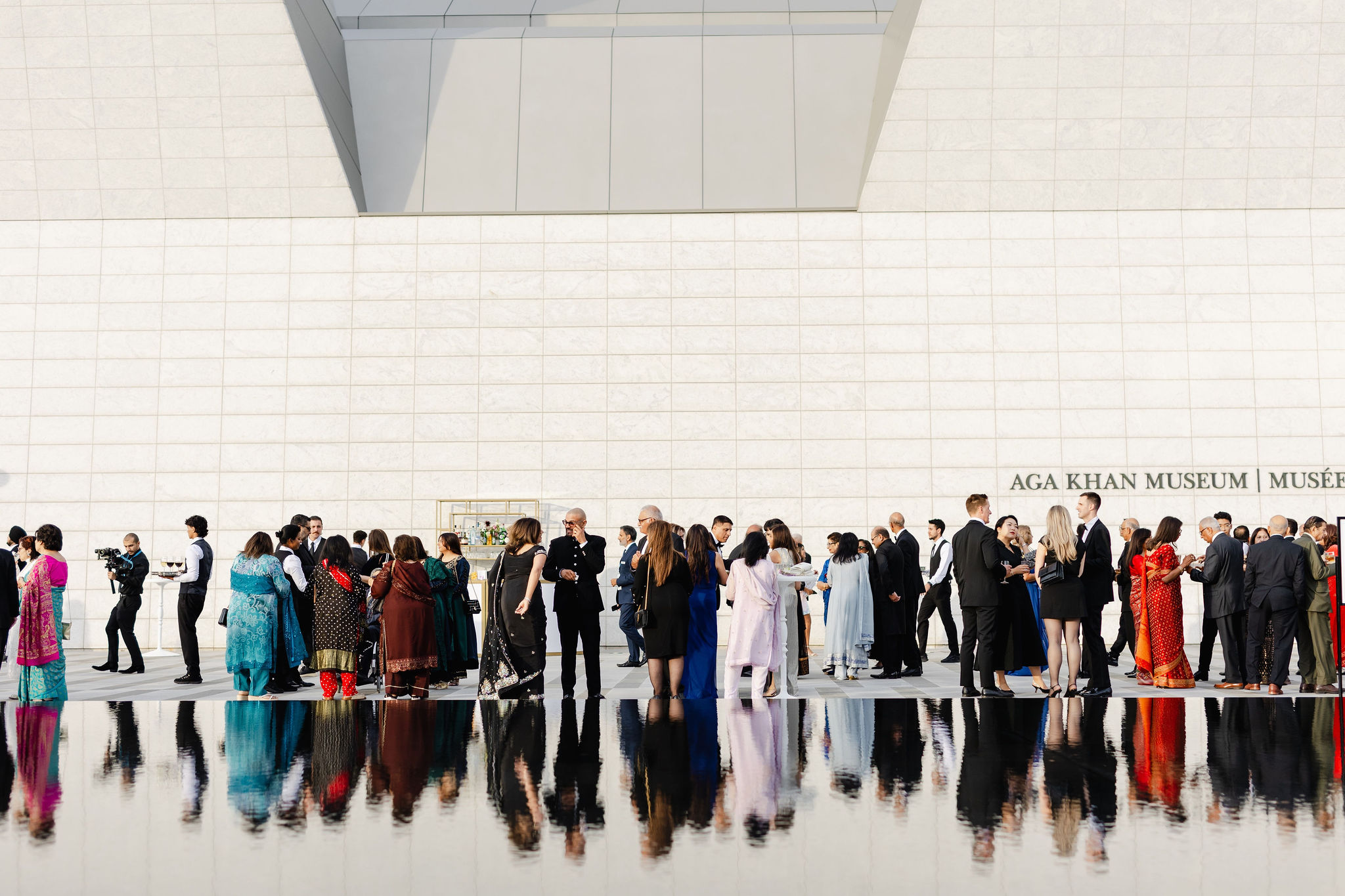 A diverse group in formal attire gathers outside the Aga Khan Museum, their reflections elegantly captured on a glossy surface, showcasing the artistry of corporate photography.
