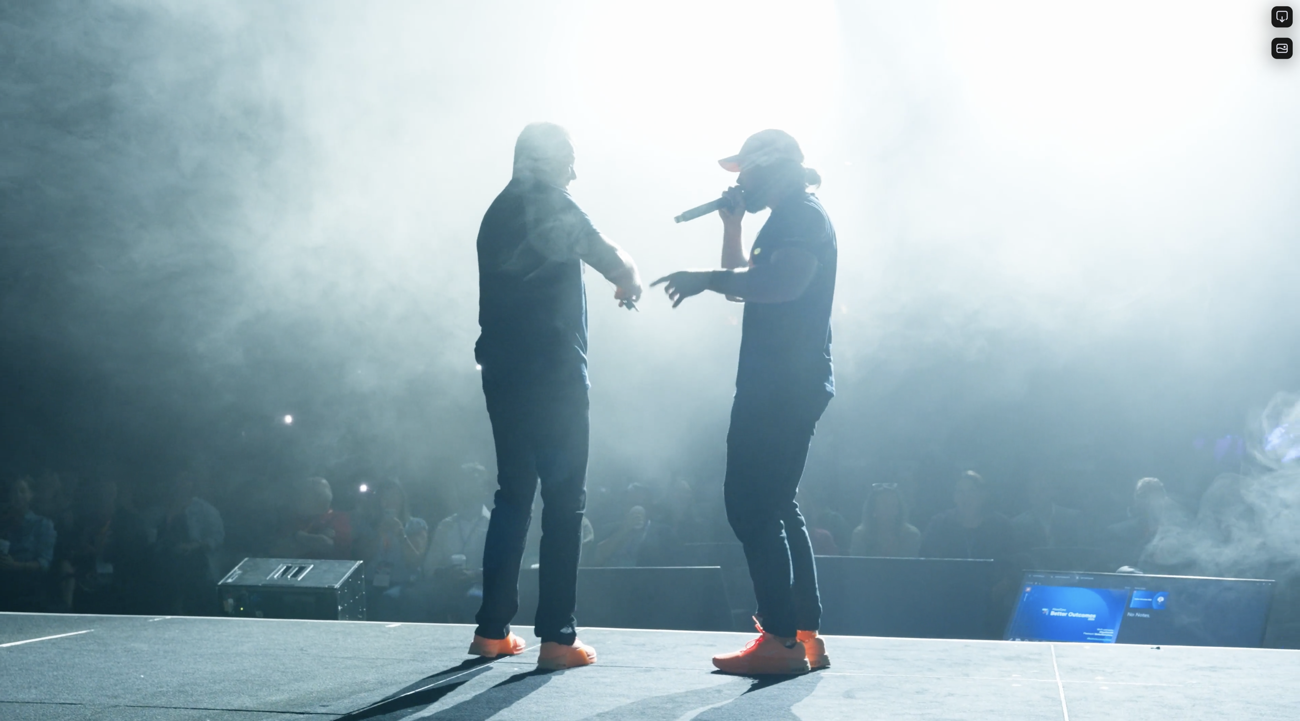 Amidst the haze of smoke effects and bright lights, two performers take the stage with microphones in hand, embodying a scene straight out of a corporate photography shoot.