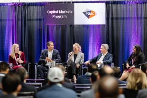 Five panelists are seated on stage, captured in sharp detail by business photography, participating in a discussion under a "Capital Markets Program" sign at a PDAC event, with an engaged audience visible in the foreground.