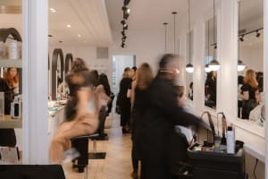 A busy hair salon with stylists working on clients, products on shelves, and several people reflected in large mirrors along the wall—an ideal setting for capturing dynamic brand videography.