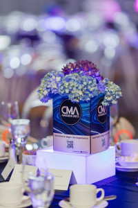 A table centerpiece with blue hydrangeas and a CMA Awards 2023 sign, surrounded by glassware, teacups, and place cards at a formal event.