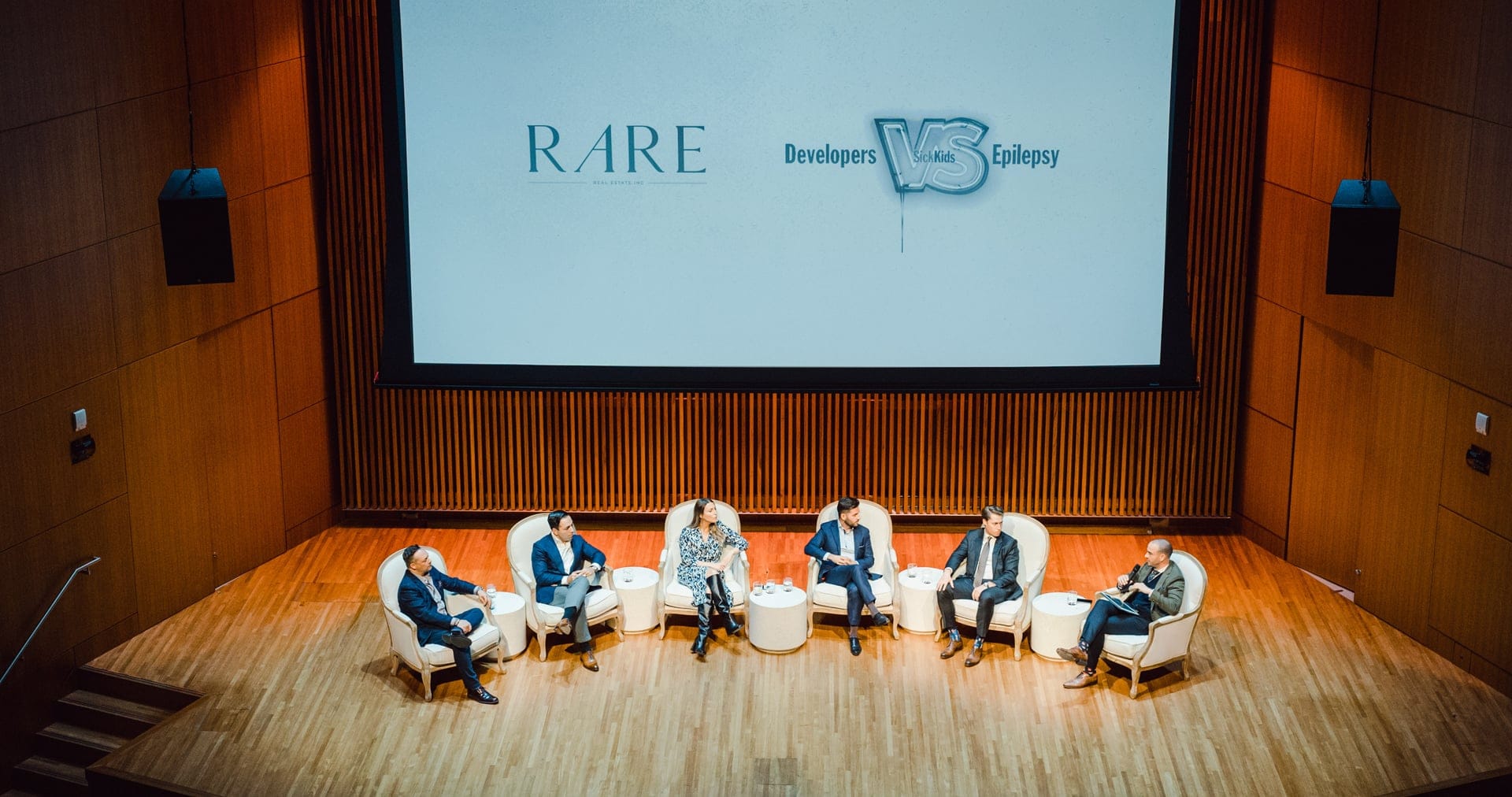 Six people from the creative team sit on stage in white chairs for a panel discussion in an auditorium, with a screen behind them displaying "RARE" and "Developers VS Epilepsy.