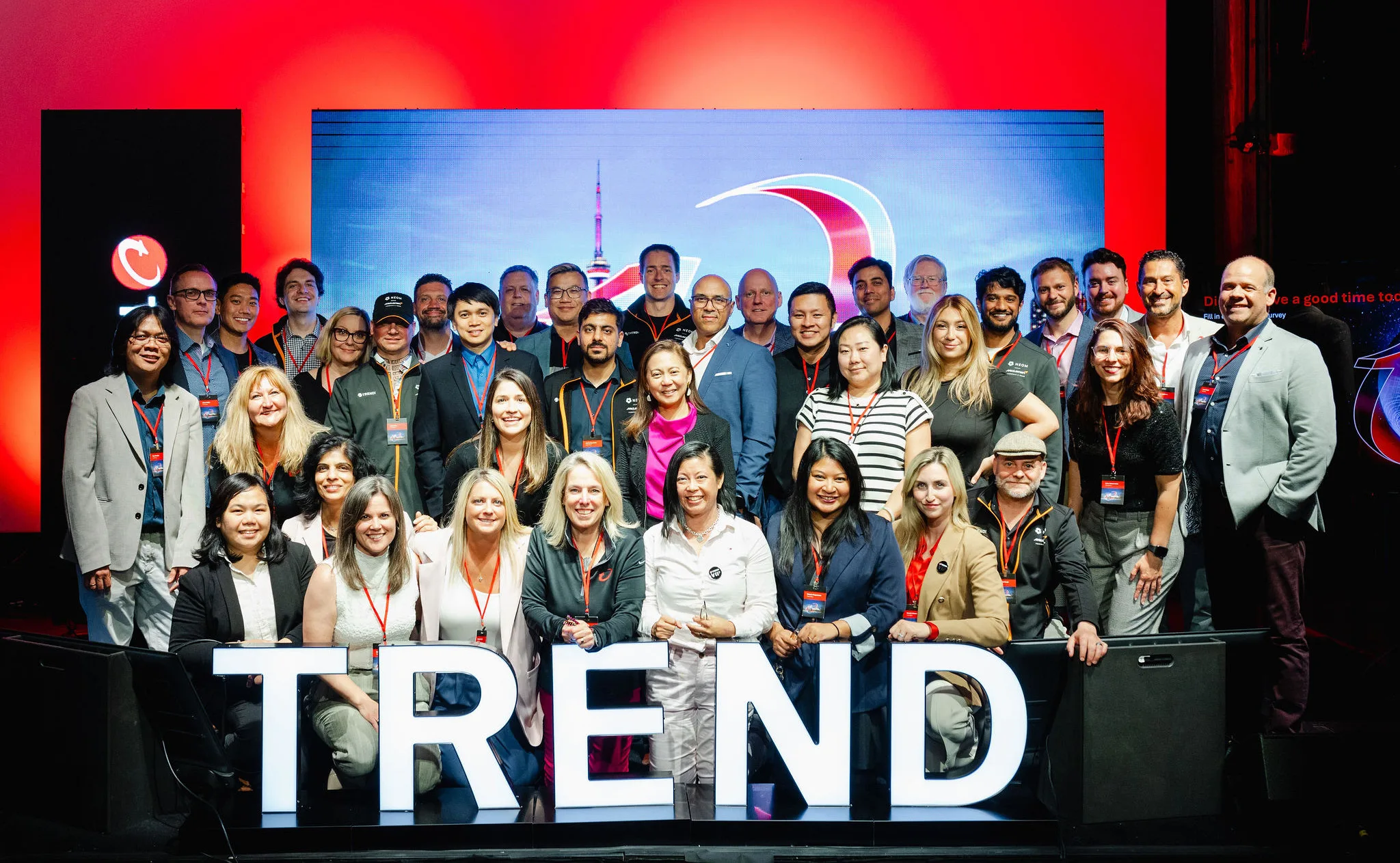 A group of people pose together on stage in front of a red and blue backdrop, standing behind large illuminated letters spelling "TREND"—a dynamic example of event photography capturing the moment.