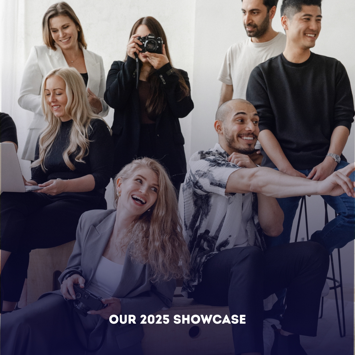 A group of seven people, some seated and some standing, interact and smile in a bright room, captured in a modern corporate photography style. Text at the bottom reads: "OUR 2025 SHOWCASE.