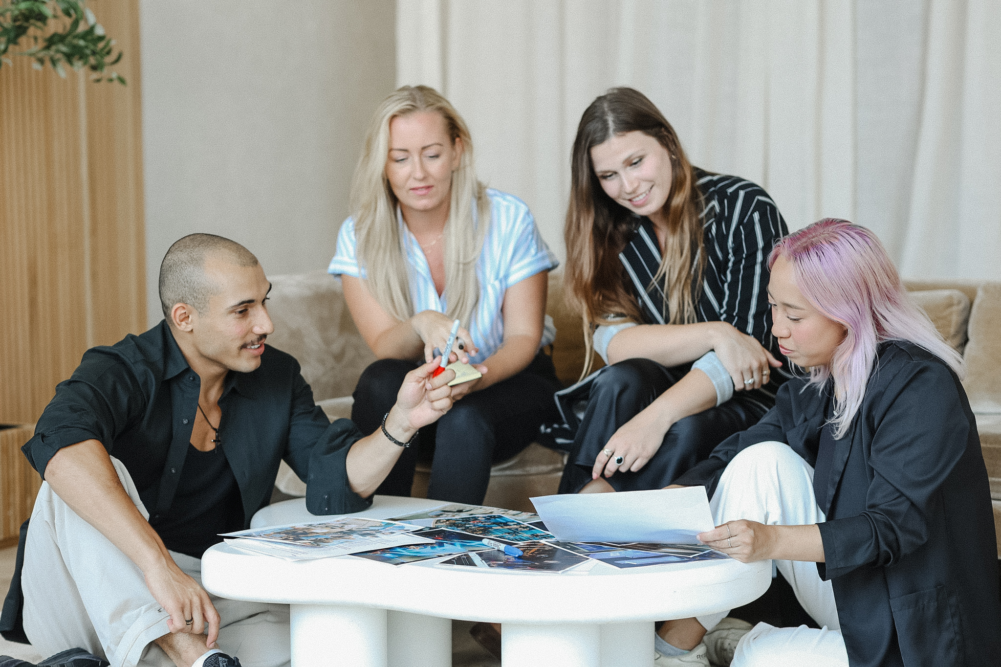 Four people sit around a low table looking at photos and papers, engaged in discussion about lessons learned from their recent content shoot in a casual indoor setting.